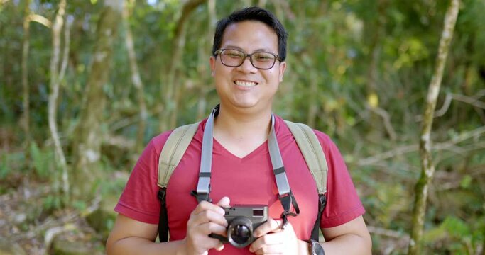 Close up, Portrait Young tourist man wearing casual clothing and eyeglasses with backpack holding digital camera in hands smile and looking to camera
