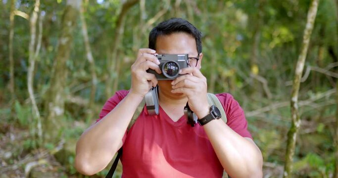 Close up, Portrait Young tourist man wearing casual clothing and eyeglasses with backpack raise up digital camera in hands take a photo with smile and looking to camera