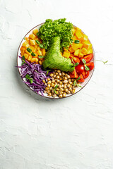vegan, detox Buddha bowl with avocado, tomato, red cabbage, chickpea, fresh lettuce salad, pumpkin, persimmon on a light background, vertical image. top view. place for text