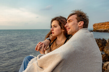 Portraits of lovers, romantic couple of lovers hugging, kissing, touching, eye contact at sunset, sunrise against the background of the sea, sun, clouds in fiery red, orange colors