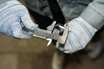 gloved hands hold a drill, the worker measures the diameter of the drill. close-up