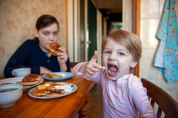 Toddler girl with older sister at   breakfast table eating pancakes.