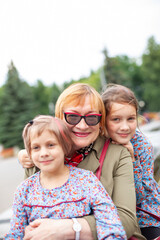 Fototapeta premium Old woman hugging granddaughters at fountain in park