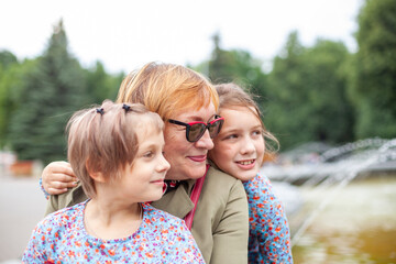 Old woman hugging  granddaughters at fountain in   park