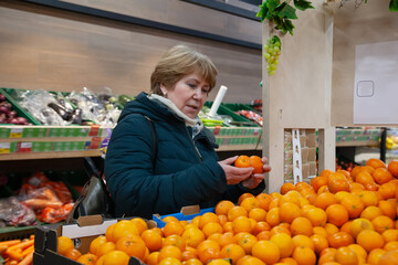Smiling senior woman picking apple at the grocery shop