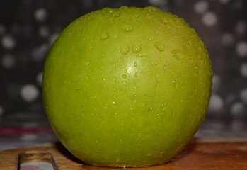 a green ripe apple in drops of water close-up.