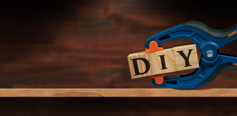 Close-up of a spring plastic clamp and text Diy (do it yourself), made of wooden blocks, above a wooden shelf or workbench with copy space.