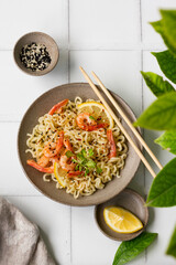 Bowl of instant noodles with shrimp, lemon, sesame seeds and chopsticks. Top view. Asian food.