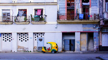 A yellow coco taxi in contrast of a old house facade in the streets of Havana in Cuba