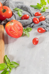 Large variety of tomatoes on rustic kitchen counter. Preparation of tomato sauce with onions and basil