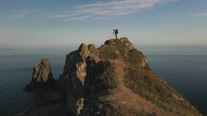 A photographer with a tripod standing on top of a mountain with an epic view of the mountains and the sea. Aerial drone shots