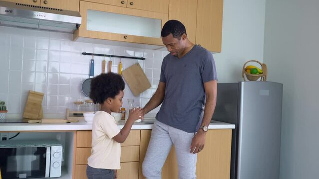 Healthy Black family Time. Handsome Afro American father pouring milk into his little cute boy while standing in modern kitchen. Happy child and parent spend time together.