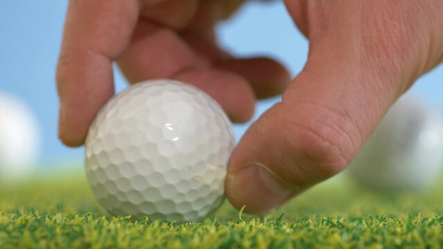 Male hand positioned golf ball on artificial lawn at indoor sport hall,macro