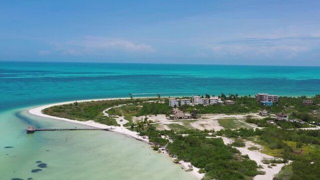 Flying towards the horizon line with a turquoise sea in the background. A small peninsula with some buildings and a jet ski passing by. Holbox, Mexico.
