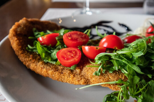 Fried breaded Milanese cutlet served with fresh cherry tomatoes and rocket