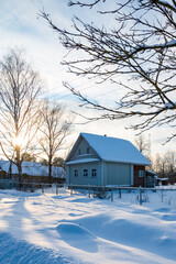 Beautiful winter landscape with wooden house in countryside on a sunny day. Trees and house are covered with snow. The sun is shining brightly. Winter day in village