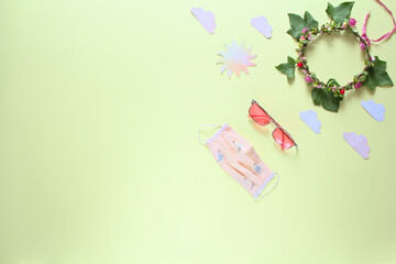 The concept of positive thinking during the covid-19 pandemic. Reusable mask, pink glasses, sun and a wreath on an yellow background. Copy space, flat lay.