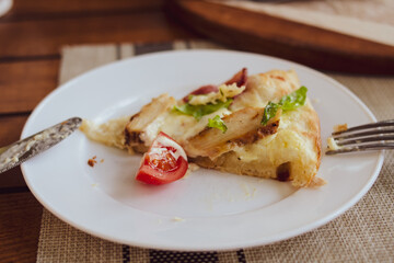 A piece of pizza with tomatoes, cheese and bacon on a white plate close-up.