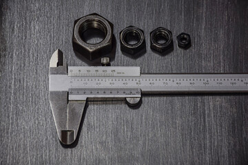 Vernier Calipers are mounted on a gray, black metal plate on top with various sizes of screw nuts. sorted from small to large