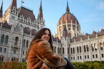 Beautiful happy Caucasian woman in winter clothes in front of the Hungarian parliament in Budapest