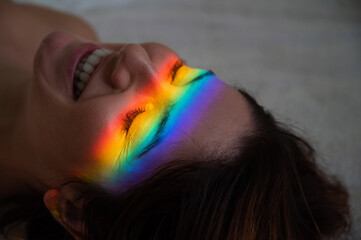 Close-up portrait of smiling woman with ray of rainbow light on her face. 
