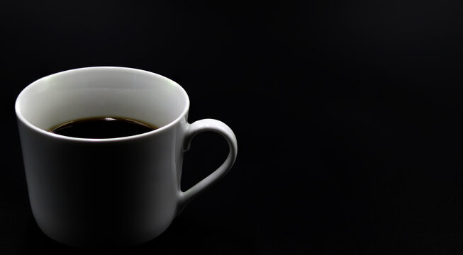 Cup of coffee on a black background located on the left of the image, for copy space