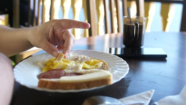 Man has breakfast fried eggs, becon and toast in outdoor cafe. Plate with delicious food
