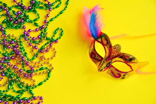 Multicolored beads and carnival mask on yellow background. Mardi Gras concept. Fat Tuesday symbol.
