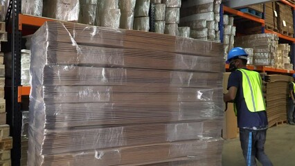 A male worker inside a warehouse, shifting a pallet loaded with cardboard boxes on its axis and moving it to a different area. Handheld shot.