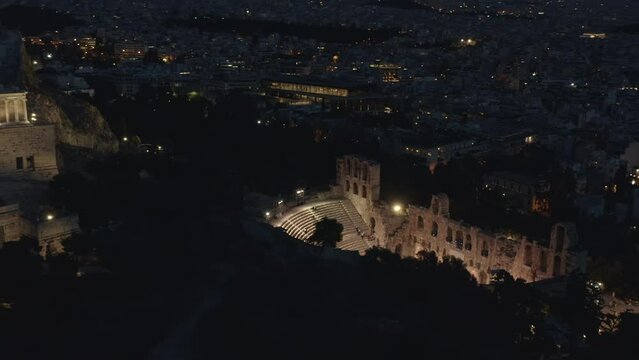 Athens Greece Aerial v37 birds eye view drone fly around illuminated odeon of herodes atticus, stone roman theater at the slope of acropolis, tilt up reveals night cityscape - September 2021