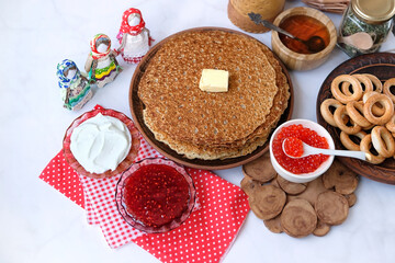 Pancakes, red caviar, sour cream, jam, honey, bread bagels, folk dolls on light marble background. Maslenitsa holiday, pancakes week. slavic festival meal. 