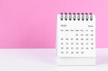 June 2022 desk calendar on white table with pink background.