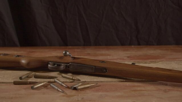 wide Dolly out of live ammunition lying in front of loaded WW2 era rifle on wooden surface