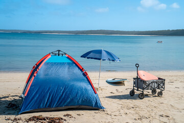 Outdoor beach cart wagon and beach umbrella on a sandy beach near the ocean. Family vacation holidays - obrazy, fototapety, plakaty