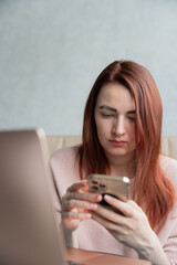 Redhead young woman sitting on sofa with laptop and smartphone.