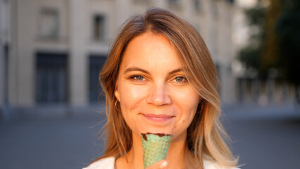 Beautiful woman eating ice cream in the city park in summer bright day. Outdoor walking, relax and leisure in nature in public park