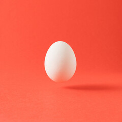 Minimal easter composition with levitating white egg against pastel red background.