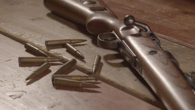 High angle dolly of Live ammunition lying in front of loaded WW2 era rifle on wooden surface