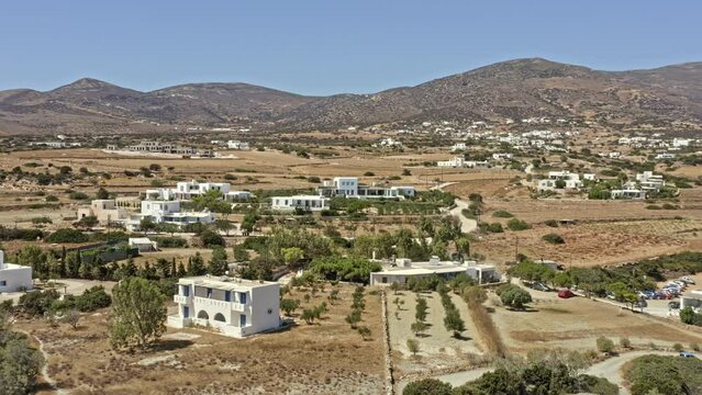 Paros Greece Aerial v6 drone reverse flying shot overlooking scattered coastal homes, panning reveals secluded paralia lolantonis beach with beautiful mountainscape background - September 2021