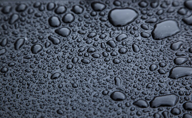 Drops of rain on a black rubber surface close-up.