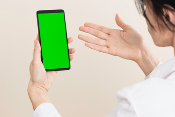 Upset, afraid, excited, upset woman holding smartphone with blank green screen chromakey background. Rear view