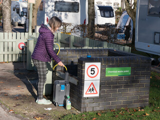 A lady at a chemical waste point on a campsite uses a hosepipe to put water into her portable...