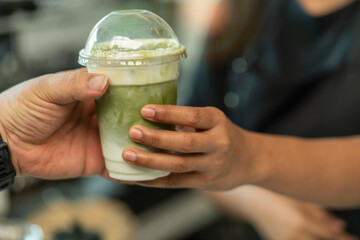 Female barita brews iced matcha green tea with milk and delivers the drink to the customer's hand. 