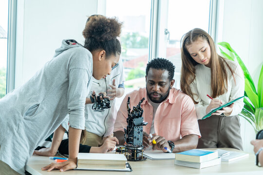 group of international students of Asian, African American youths and white girls sit and study with educational robot hands guided by teachers in school classrooms.