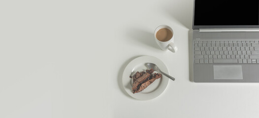 chocolate brownie and coffee next to laptop on white background