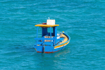 Small blue and yellow boat, lost and empty in the middle of the sea, surrounded just by water.