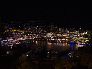 Fototapeta premium Stunning night view of the downtown of Monaco at the mediterranean coast with funfair and yacht boats moored in marina Port Hercule with buildings.