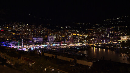 Beautiful night view of the harbor of Monaco (Port Hercule) at the French Riviera with colorful funfair surrounded by illuminated apartment buildings.