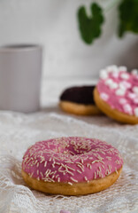 Sweet round donut with pink glaze and white sprinkles and cup of tea on a white background. Side view. Dessert and bakery concept.