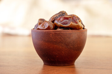 Dry tasty dates in a brown ceramic cup on a blurred background